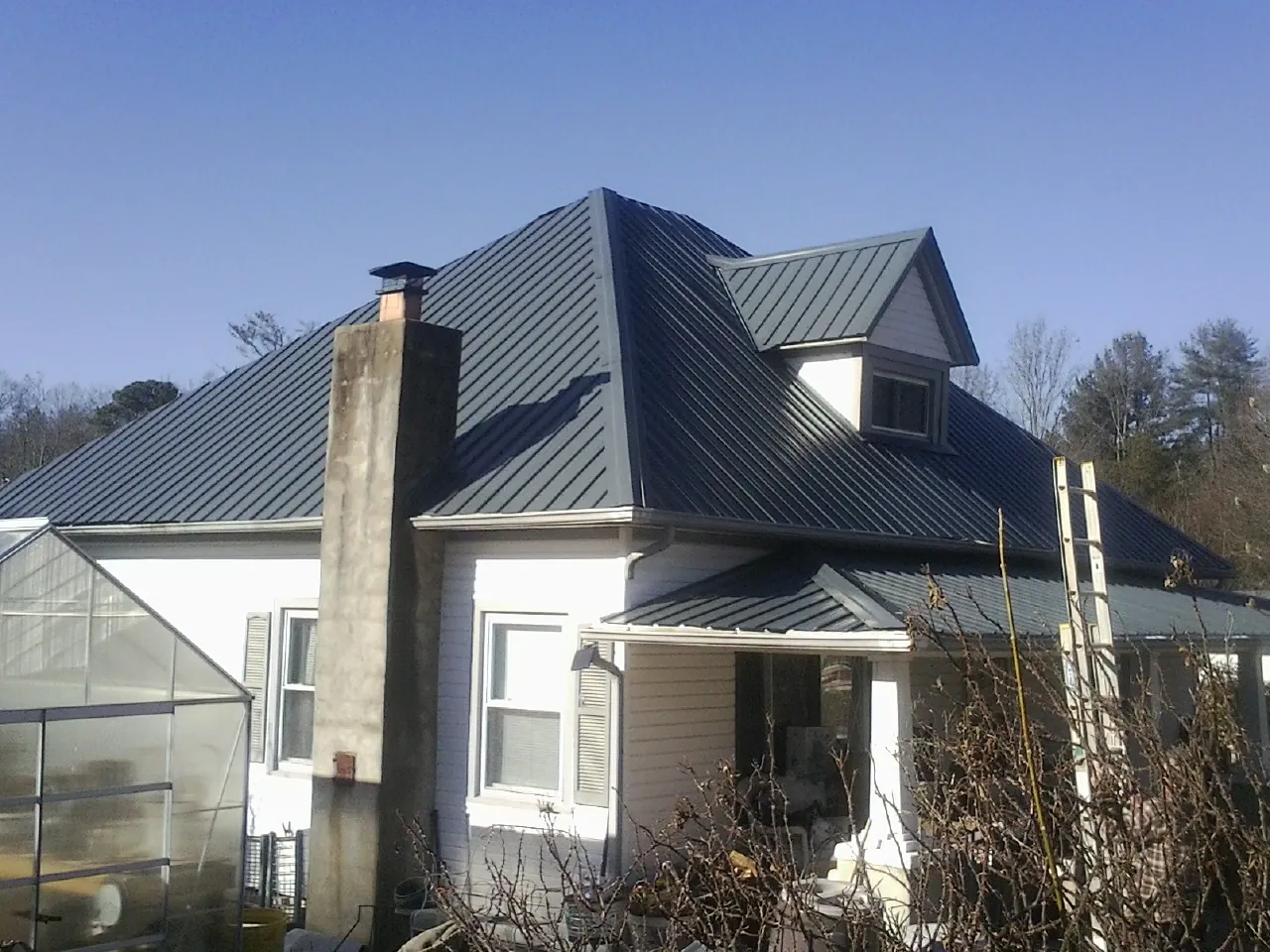Dark blue standing seam metal roof on a white farmhouse with dormer — Slate & Tile Roof Repair by Roofing Brothers in Wheelwright