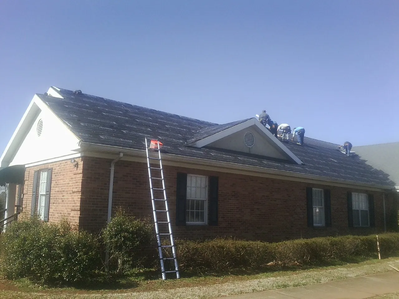 Crew tearing shingles off a brick ranch roof with a ladder set — Emergency Roof Repair work by our crew in Wheelwright